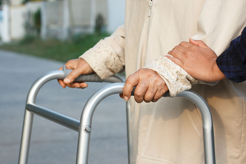 hand-of-carer-on-the-arm-of-elderly-lady-using-a-walker